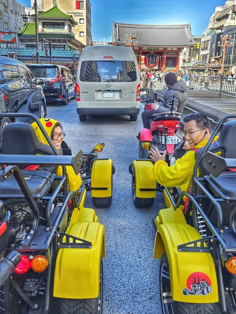 Two go-kart riders in Pikachu costumes smile while driving past Senso-ji Temple in Asakusa, Tokyo.