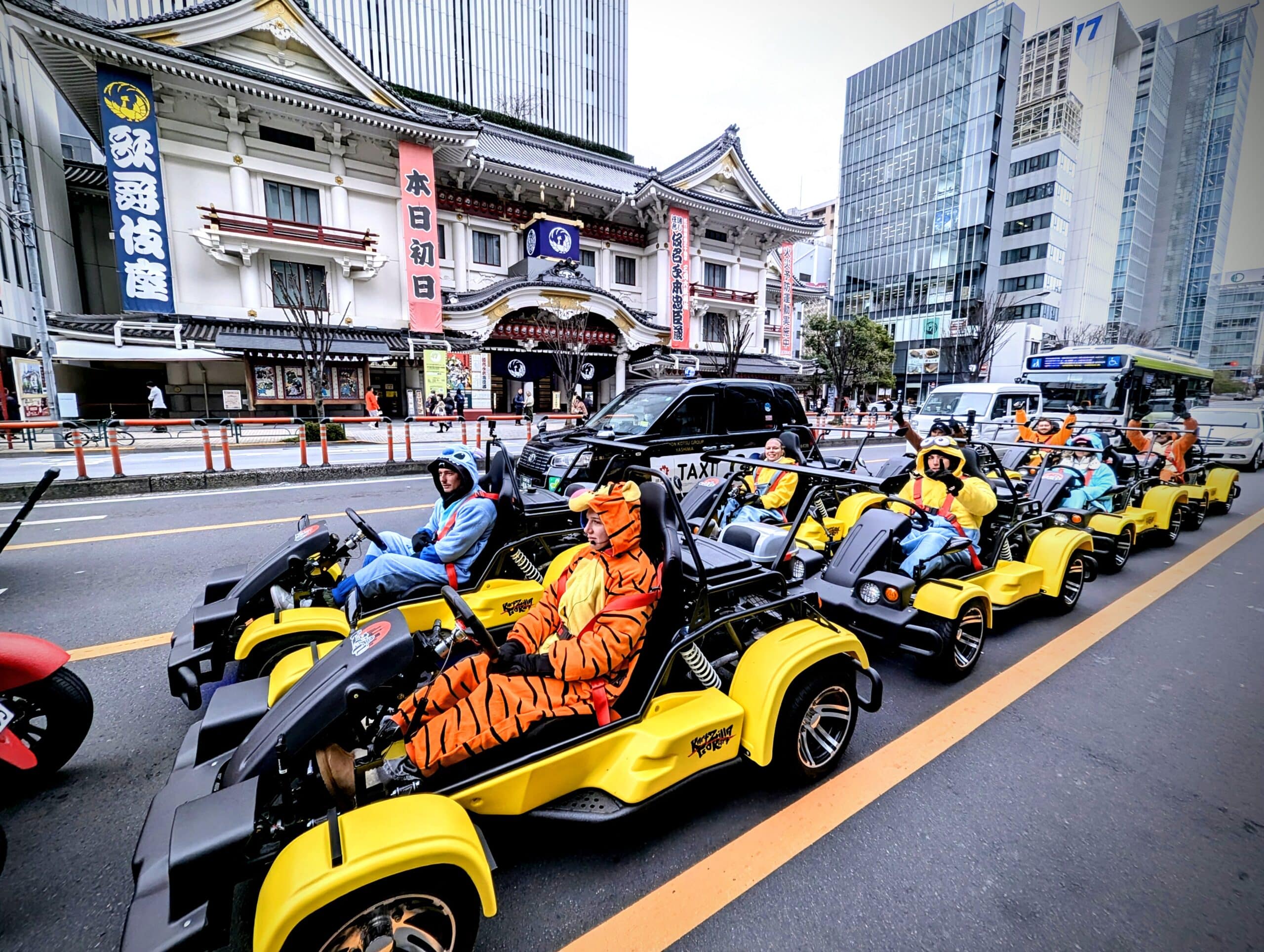 Go-kart group dressed in colorful costumes driving past Tokyo's iconic Kabukiza Theater in Ginza.