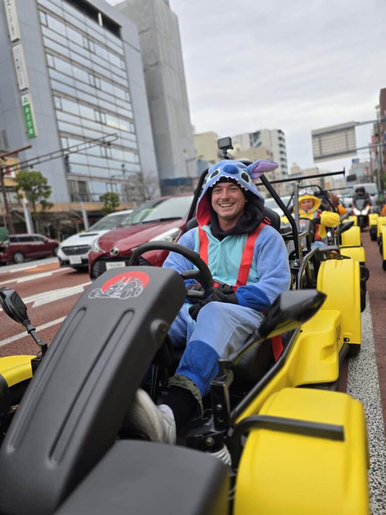 Smiling Kartzilla Go Kart rider dressed in Stitch costume cruising through the streets of Sumida, Tokyo with fellow go-karters.
