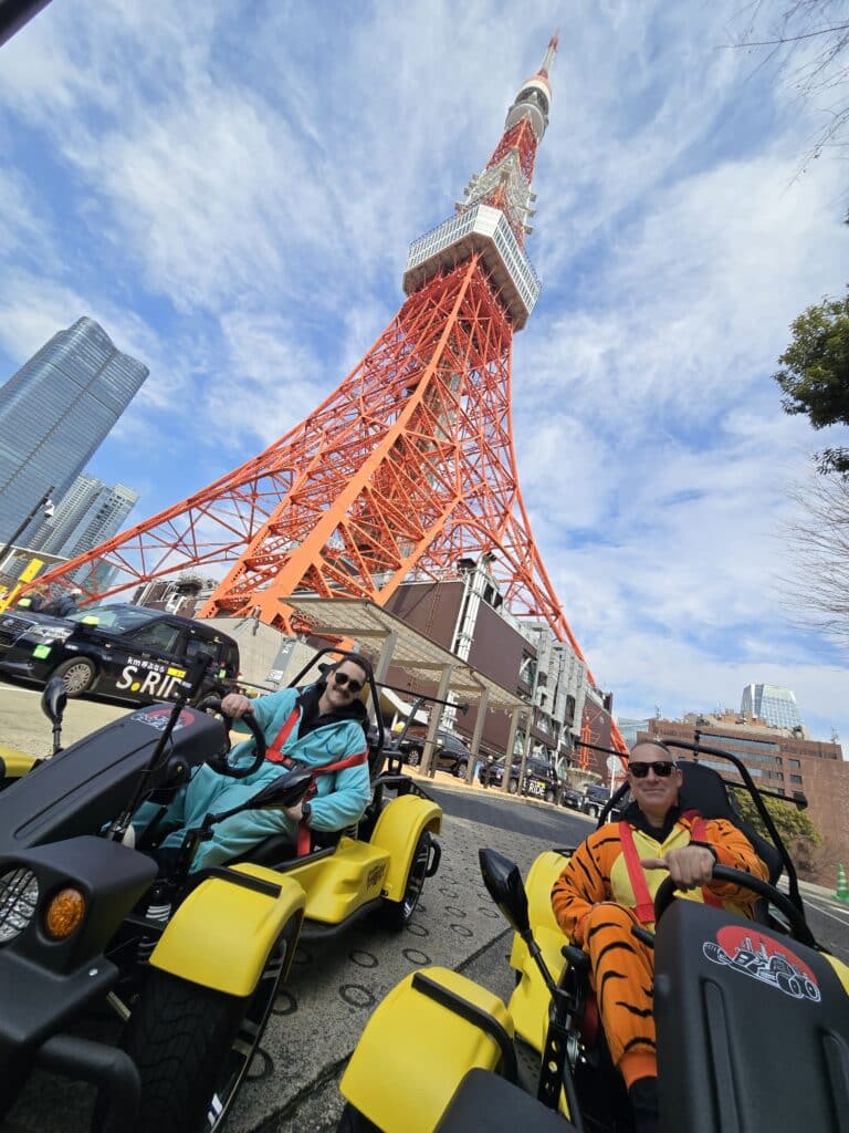 Go-kart riders in costume posing in front of Tokyo Tower during a daytime Kartzilla Go Kart tour.
