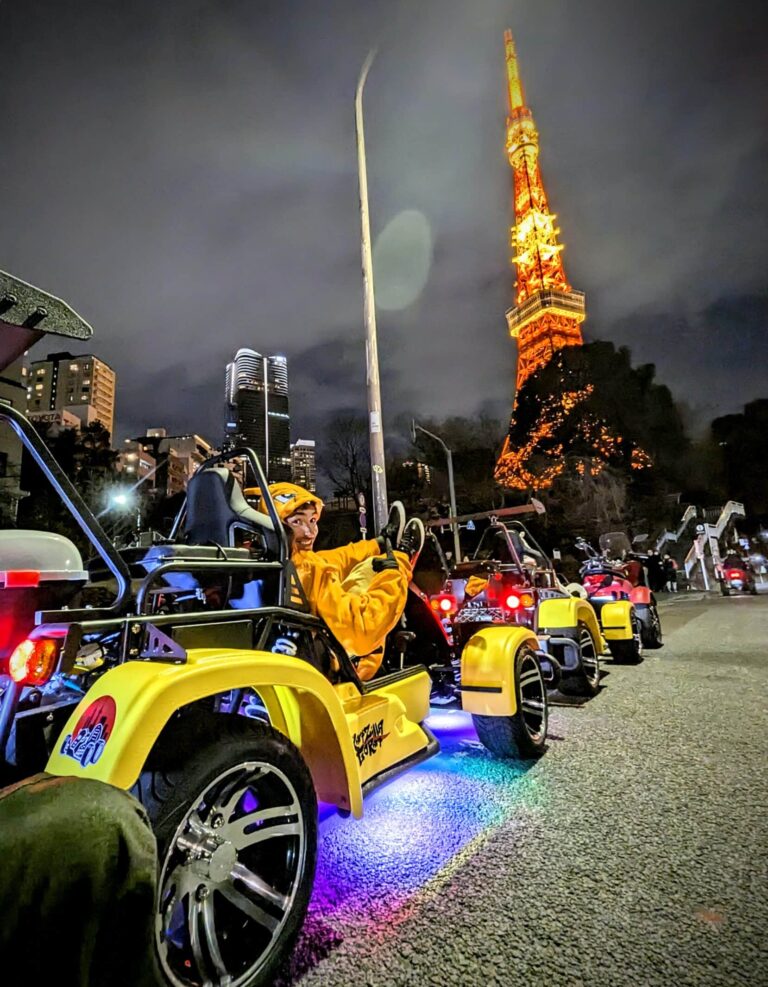 Go-kart rider in a Charizard costume cruising beneath the illuminated Tokyo Tower during a Kartzilla night tour.