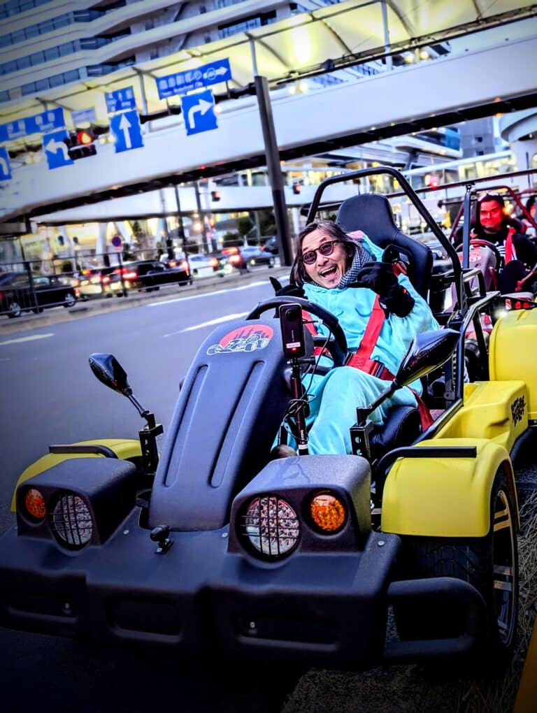 Excited go-kart rider in a blue costume near Toyosu Fish Market during a Kartzilla Tokyo street tour.