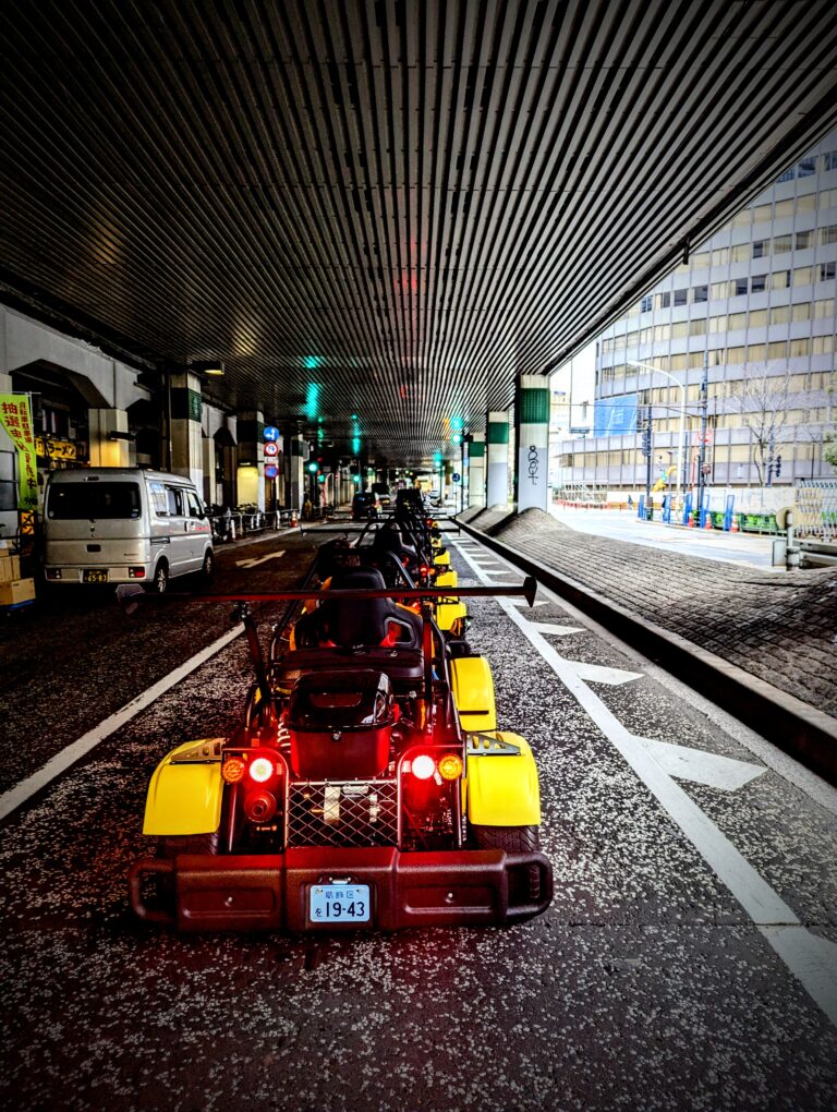 A row of yellow Kartzilla go-karts drives under a Tokyo highway overpass during a street tour.