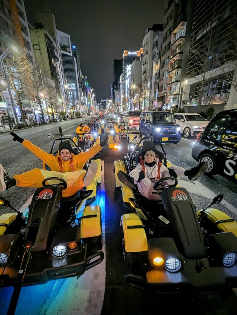 Go-kart riders with arms and feet outstretched driving through Akihabara nightlife with Kartzilla Go Kart.