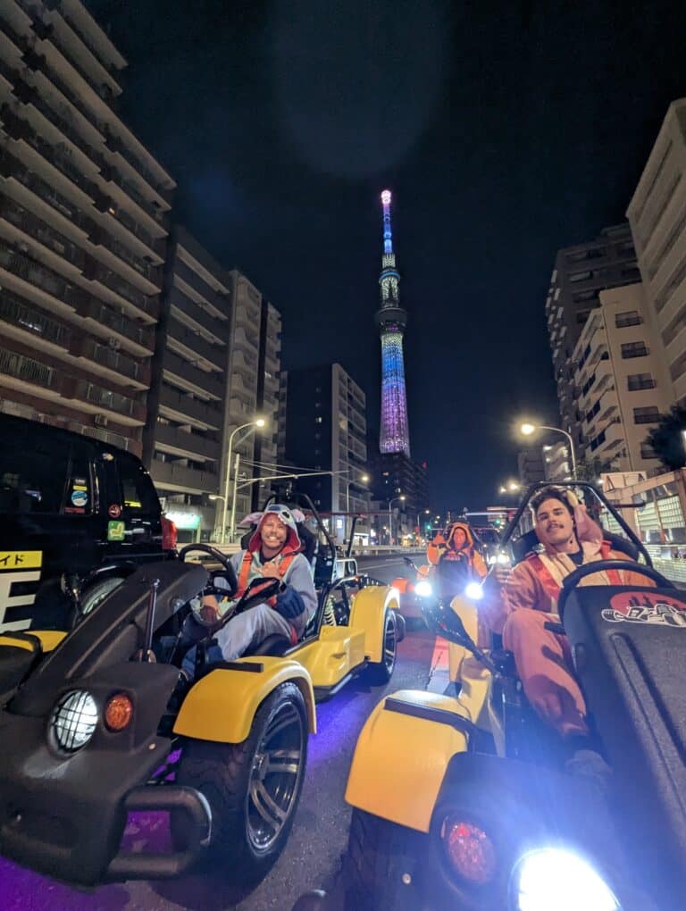 Kartzilla Go Kart riders in costume passing by a brilliantly lit Tokyo Skytree at night.