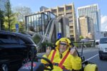 Older man in Pikachu costume smiles in a yellow go-kart with futuristic Azabudai Hills architecture in the background during a Kartzilla Go Kart tour in Tokyo.
