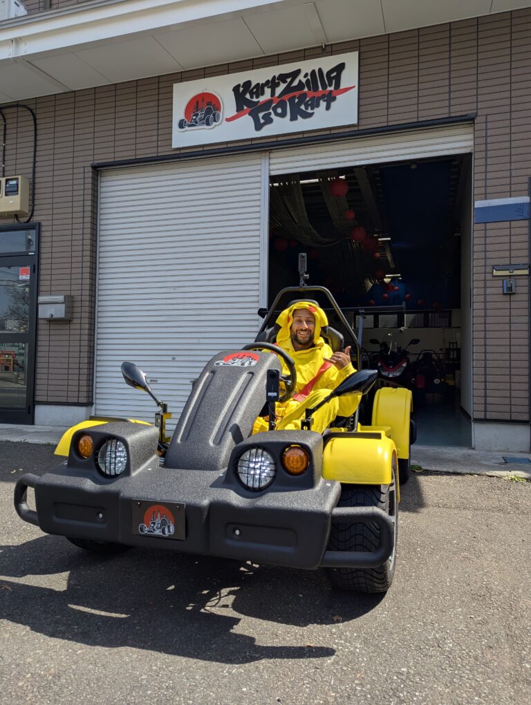 Man in Pikachu costume gives a thumbs up while sitting in a yellow go-kart in front of the Kartzilla Go Kart facility in Tokyo, Japan.