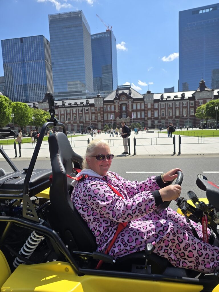 Smiling woman in a pink costume drives a yellow Kartzilla go-kart in front of Tokyo Station on a Mario Kart style street karting tour.