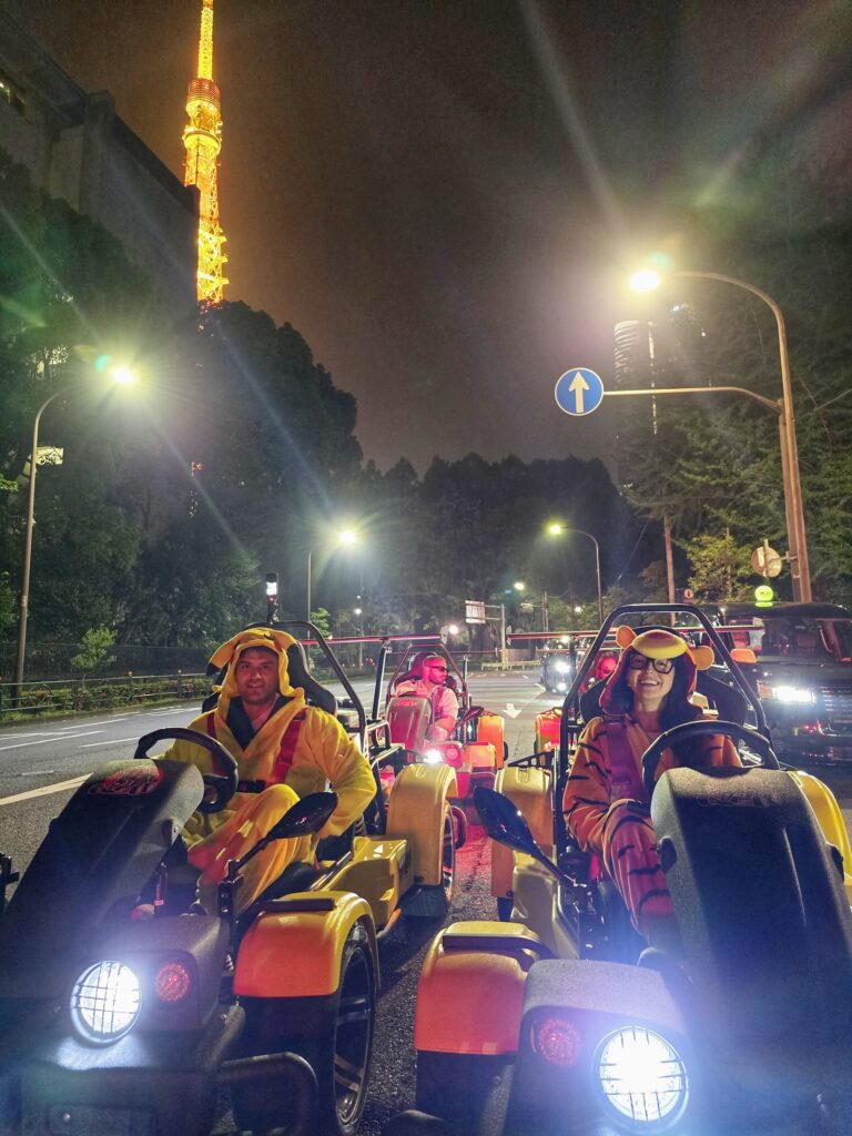 Costumed Kartzilla Go Kart riders cruising past illuminated Tokyo Tower on a Mario Kart style night tour through Tokyo streets.