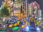 Tourists in Pikachu and Stitch costumes driving Mario Kart style street karts through Akihabara at night during a go-kart Tokyo tour with Kartzilla Go Kart.