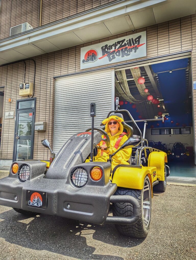 Tourist in a Pikachu-style costume smiling in a yellow Mario Kart style go-kart outside the Kartzilla Go Kart facility in Tokyo, ready for a street kart tour.