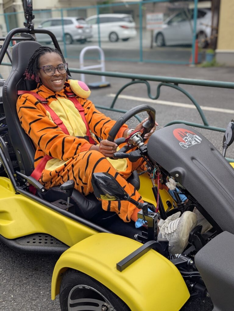 Woman in tiger costume smiling while driving a yellow go-kart during a Kartzilla Mario Kart style tour in Tokyo.