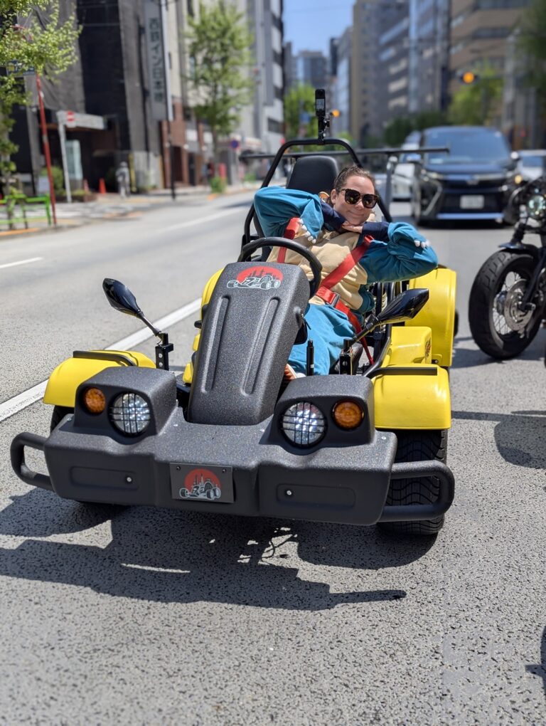 A Kartzilla Go Kart rider relaxes in a yellow street kart on a sunny Tokyo road, dressed in a Mario Kart style costume during a go-karting tour in Nihonbashi.