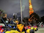 Smiling tourist in costume driving a Kartzilla Go Kart on Tokyo street at night with the illuminated Tokyo Tower in the background on a Kartzilla Go Kart tour.