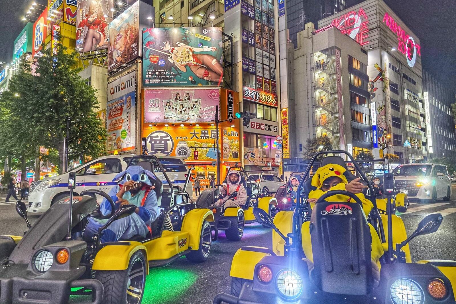 Tourists in Pikachu and Stitch costumes driving Mario Kart style street karts through Akihabara at night during a go-kart Tokyo tour with Kartzilla Go Kart.