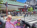 Smiling woman in a purple costume driving a street kart in front of Kaminarimon Gate in Asakusa, Tokyo, enjoying a Mario Kart style go-kart Tokyo experience.