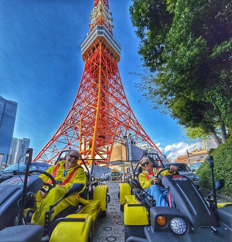 Tourists driving street-legal go-karts in costume under Tokyo Tower on a Kartzilla Go Kart tour in Tokyo